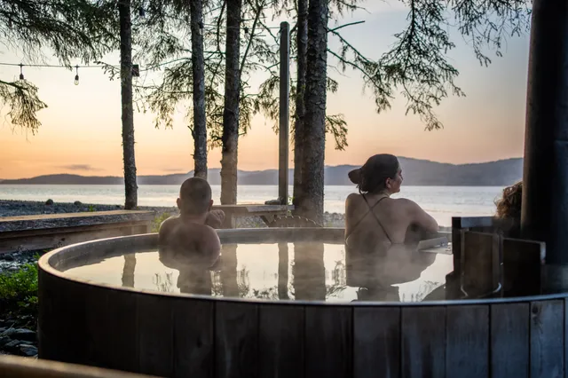 Guests in the wood-fired hot tub at sunset above the beach