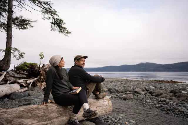 Guests resting on a driftwood log on the pebble beach