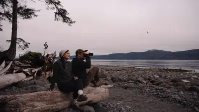 Guests resting on a driftwood log on the pebble beach